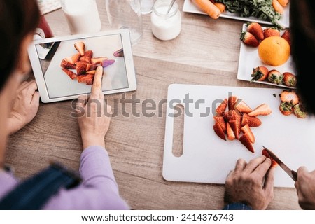 Woman taking picture with tablet while her friend chopping strawberries- partial view