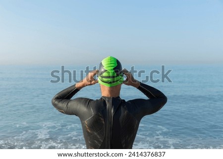 Triathlete preparing to swim- putting on swimming cap and goggles- rear view Royalty-Free Stock Photo #2414376837