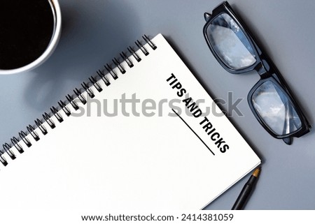 Tips and tricks text written on notepad with pen, coffee and reading glasses on a desk.
