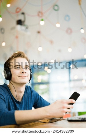 Portrait of relaxed young man listening music with headphones and smartphone in a coffee shop