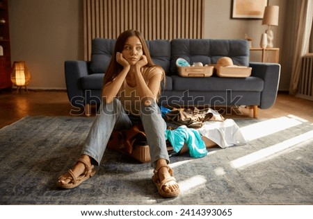 Young overwhelmed woman having trouble packing suitcase for vacation trip Royalty-Free Stock Photo #2414393065