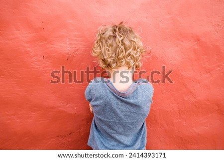 Back view of little boy standing in front of red wall Royalty-Free Stock Photo #2414393171
