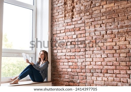 Woman sitting at home on the window sill- reading a book