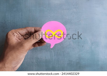 A close-up photo of a hand holding a pink speech bubble with a gold infinity symbol on it.