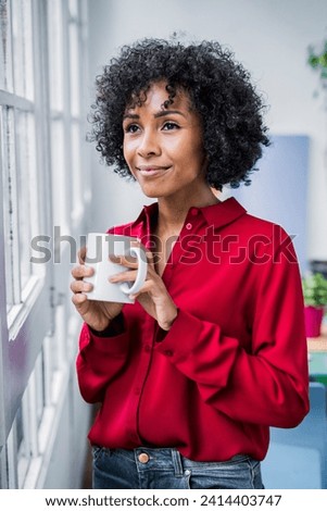 Smiling woman with cup of coffee looking out of window at home