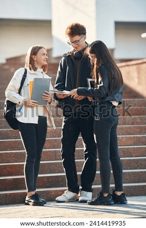 Holding notepads in hands. Three young students are outside the university outdoors. Royalty-Free Stock Photo #2414419935
