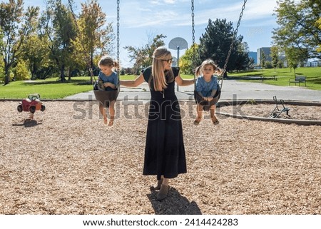 Blonde mother with girls at playground on swingset Royalty-Free Stock Photo #2414424283
