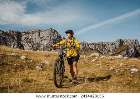 Mid adult woman holding bicycle while against mountain at somiedo natural park- spain Royalty-Free Stock Photo #2414428055