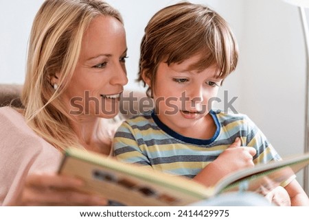 Mother and son reading a book together on couch at home