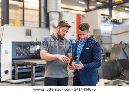 Employee explaining workpiece to businessman on factory shop floor Royalty-Free Stock Photo #2414434075