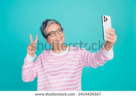 Photo of excited cheerful lady wear striped sweater spectacles tacking selfie device showing v-sign isolated turquoise color background