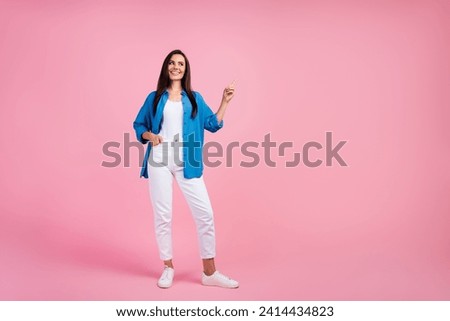 Full length photo of cheerful woman wear stylish shirt white pants look directing at promo empty space isolated on pink color background