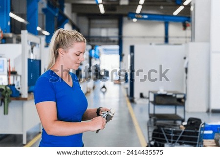 Woman measuring metal workpiece in industrial factory Royalty-Free Stock Photo #2414435575