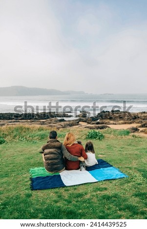 Back view of family with dog sitting on blanket at the coast Royalty-Free Stock Photo #2414439525