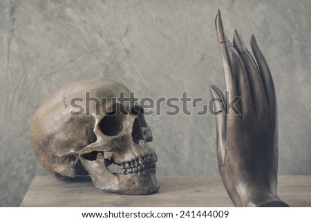still life photography : skull confront with hand of buddha image in good and evil concept in vintage color tone