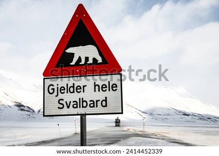 A road sign in Svalbard warning about the presence of polar bears across the Islands.  The picture also shows an incoming truck in the background.  The road is frozen.