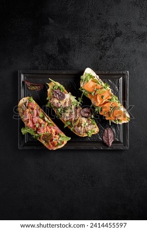 Top view of a bruschetta set with salmon, roast beef, and tuna on a black rectangular plate. Royalty-Free Stock Photo #2414455597