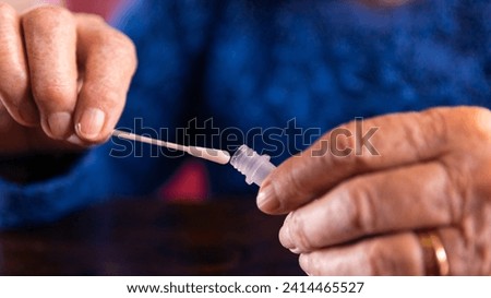Close-up of old woman taking a self swabbing home tests for Covid19 with antigen kit. Caucasian grandma introducing nasal stick to buffer dropper for check infection of Coronavirus.