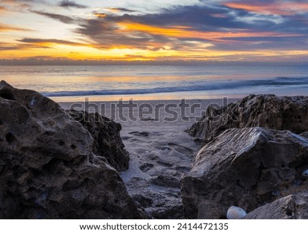 Dynamic coastal sunrise with textured rocks and soft sand, great for dynamic website headers, travel magazines, and inspirational posters.