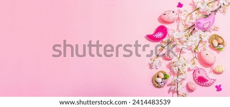 Gentle Easter composition with cherry flowers and handmade felt birds. Decorative eggs and nest, cute rabbits. Hard light, dark shadow, pink background, banner format