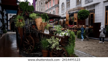 a quaint urban alleyway enhanced with rustic wooden carts overflowing with an array of vibrant flowers and plants, creating a charming and green atmosphere.