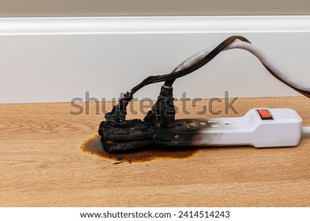 Electrical surge protector outlet and extension cord fire. Electricity safety, fire hazard and circuit overload concept. Royalty-Free Stock Photo #2414514243