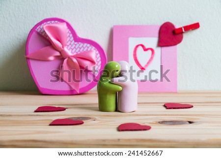 Hugging ceramic dolls on wooden table over paper photo frame background, Valentine concept 