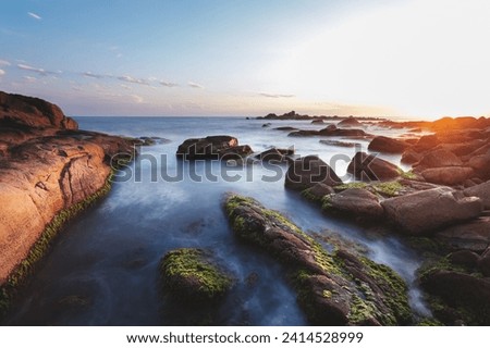Wave water flow between mossy rocks in setting sun landscape in long exposure photography