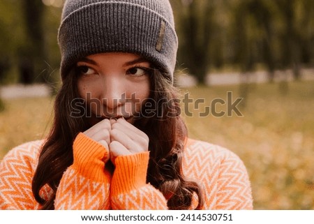 Caucasian woman walking outdoor, portrait of young european lady in warm sunny autumn park season, fall, yellow orange red leaves, feeling cold, rubbing hands blowing on palms
 Royalty-Free Stock Photo #2414530751