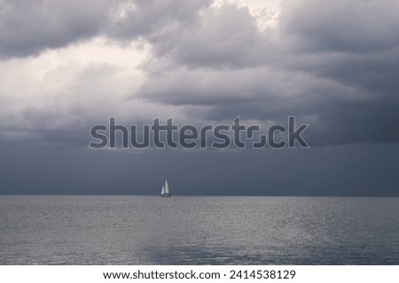 Gray horizon, clouds, water surface and a single sailboat with white sails.
Too much gray for sailing.