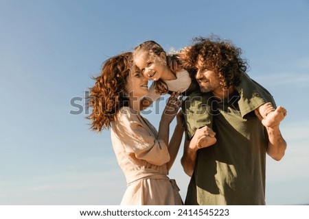 Happy family having fun on beach during holidays. Spouses father and mother parents holding their little kid piggyback on weekend walking along lake river Royalty-Free Stock Photo #2414545223