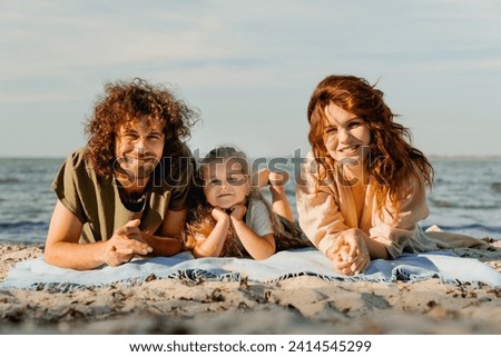 Happy family having fun relax and lying on a blanket on sunny beach. Parents father and mother and daughter kid child spending time together outdoors
