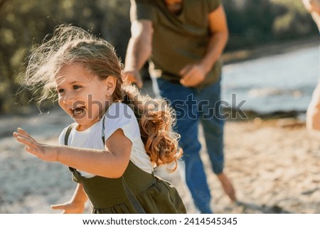 Close up shot of little girl running on beach with parents. Daughter playing with her family outdoors. Family time together