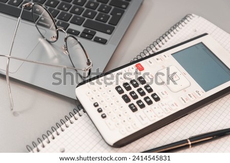 computer, calculator and notepad with pen on gray background
