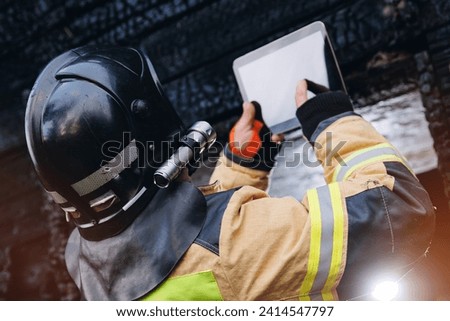 Fireman inspector officer inspects burnt house, take photo on tablet for report of investigating incident fire. Control safety after burning apartment. Royalty-Free Stock Photo #2414547797