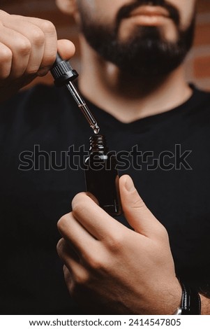 Happy male use cosmetic pipette with oil for beard growth, barber shop skin and hair care for man. Royalty-Free Stock Photo #2414547805