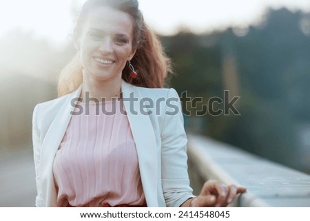 Portrait of smiling middle aged woman in pink dress and white jacket in the city on the bridge. Royalty-Free Stock Photo #2414548045