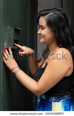 Portrait of beautiful young woman with black hair ringing the doorbell of a house and smiling. Person traveling.