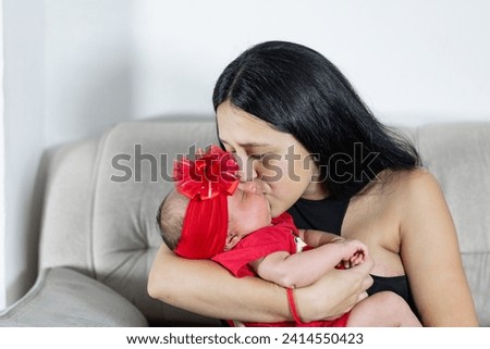 young latina woman holding her baby while kissing her on the cheek with a lot of happiness and pride of being a mother.