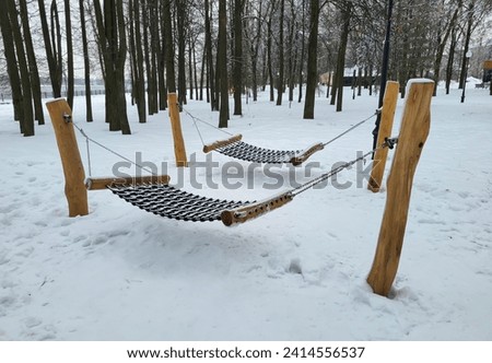 Wooden swing outside in winter under a thick layer of snow. The theme of winter cold and entertainment.