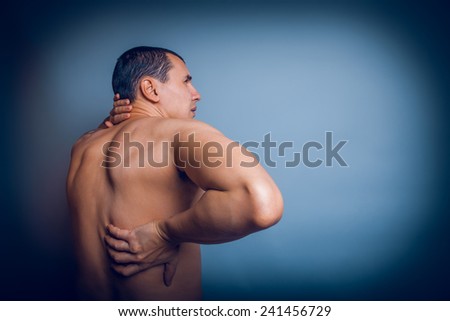 the man of European appearance brunet holding hands behind his back feels pain in the back cross process Royalty-Free Stock Photo #241456729