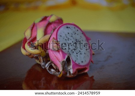 A tasty white meat pitaya broken in half vertically along with another ripe fruit on the rustic wooden board