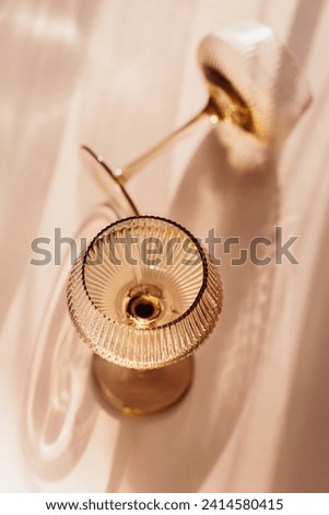 Two glasses with white wine placed on light beige background with shadows and fantastic highlights and reflecting bright sunlight in daytime