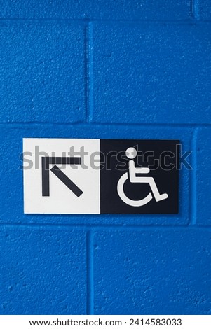 Handicap sign with an  arrow on a blue, brick wall