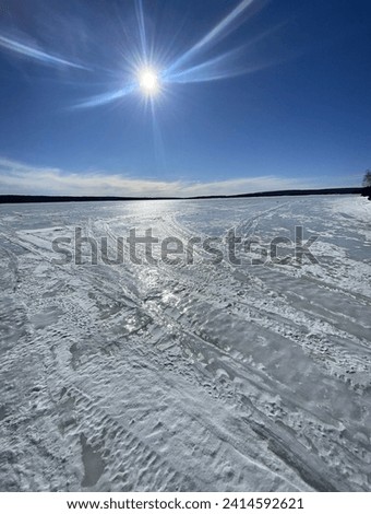 Hey, beautiful picture of a ice covered pond with blue skies, sparkling sun, and slight cloud with land on the horizon. Royalty-Free Stock Photo #2414592621