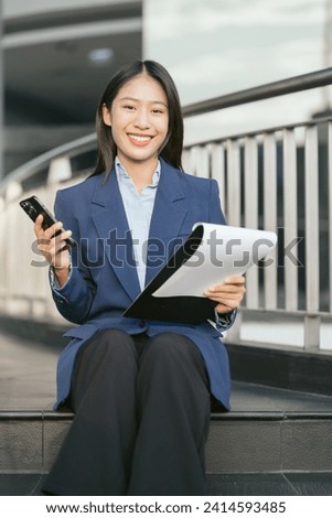 Portrait of a successful business woman using smartphone and digital tablet in front of modern business building.