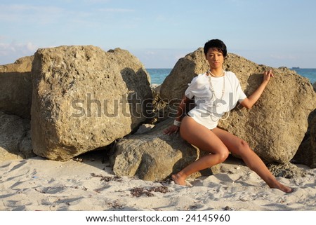 Young woman posing by boulders on the beach