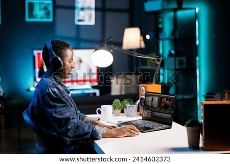 Black woman wearing wireless headset for listening and editing audio and video footage on her personal computer. Freelancer with headphones and laptop, utilizing modern technology in content creation.