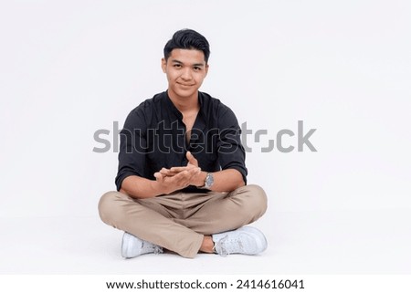 A young southeast asian man sitting indian style, making a proposition. Studio shot isolated on a white background.