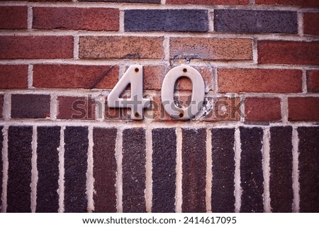 The image shows the number 40, with digits in metal affixed to a brick wall, exhibiting a variety of warm tones and textures.